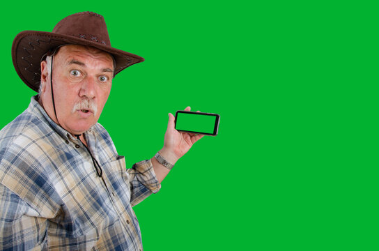 Against a green backdrop, an elderly farmer holds a smartphone with a green screen, his face showing clear disappointment, highlighting the generational gap in technology usage or something else.