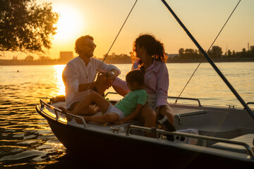 Family enjoying a sunset boat ride on a calm river. The sun is setting in the background, casting a...
