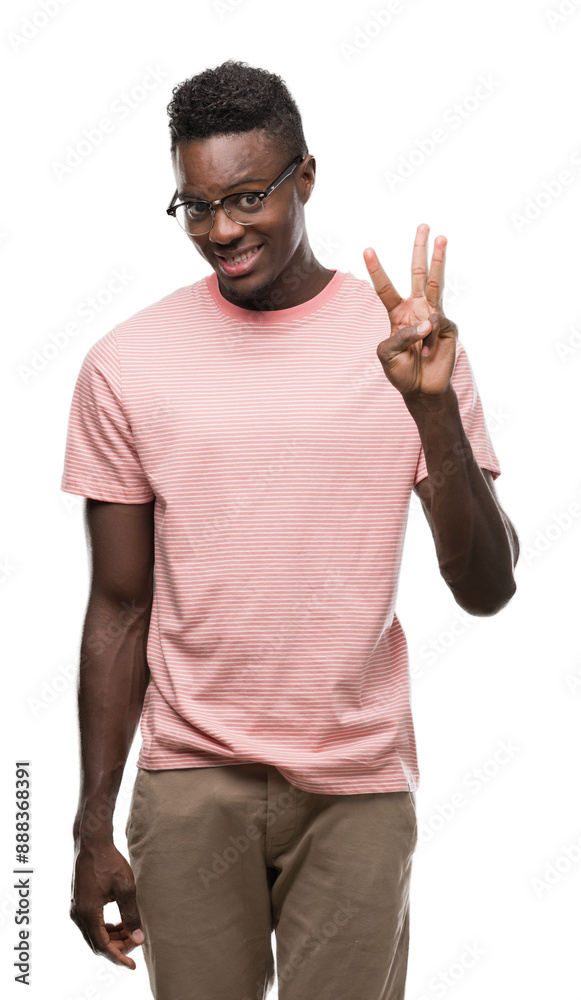 Sticker Young african american man wearing pink t-shirt showing and pointing up with fingers number three while smiling confident and happy.