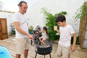 Father and son grilling together in a cozy backyard setting while other family members relax and...