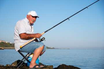Old man sitting on his chair on the shore fishing