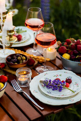 Beautiful elegant outdoor arrangement in meadow with purple blue lupins. Perfect date, private wedding or romantic marriage proposal. Summer, sunset, golden hour. Appetisers, rose wine, strawberry