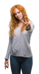 Young redhead woman smiling looking to the camera showing fingers doing victory sign. Number two.