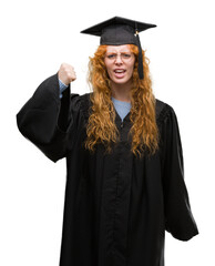 Young redhead student woman wearing graduated uniform annoyed and frustrated shouting with anger, crazy and yelling with raised hand, anger concept