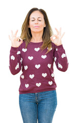 Beautiful middle age woman wearing hearts sweater over isolated background relax and smiling with eyes closed doing meditation gesture with fingers. Yoga concept.