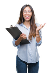 Young asian business woman holding clipboard over isolated background very happy and excited, winner expression celebrating victory screaming with big smile and raised hands