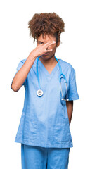 Young african american doctor woman over isolated background smelling something stinky and disgusting, intolerable smell, holding breath with fingers on nose. Bad smells concept.