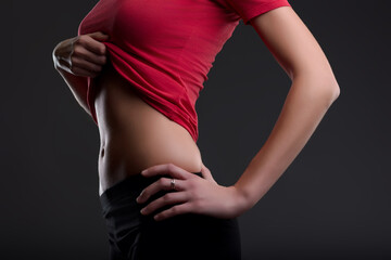 Young fit woman showing her belly on grey background