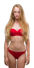 Blonde teenager woman wearing red bikini skeptic and nervous, frowning upset because of problem. Negative person.