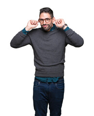 Fototapeta premium Young handsome man wearing glasses over isolated background Smiling pulling ears with fingers, funny gesture. Audition problem