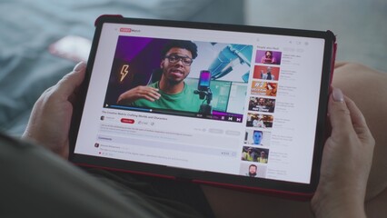 Caucasian woman watches educational video of blogger about 3D modeling using tablet computer while lying on sofa. Tablet screen shows video hosting website interface with video content. Close Up.