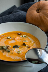 Orange pumpkin cream soup puree, autumn, a spicy, traditional dish with spices seeds, and grains prepared on the eve of Thanksgiving 2023. On a dark background with a spoon and squash. Close-up
