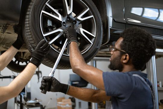 Mechanics using tools to fix car wheel in auto repair shop. Teamwork in automotive maintenance and tire repair. Close-up of workers' hands and tools.