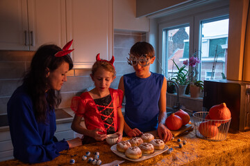 Mother, daughter and son in Halloween costumes draw skulls with cocoa powder and powdered sugar on...