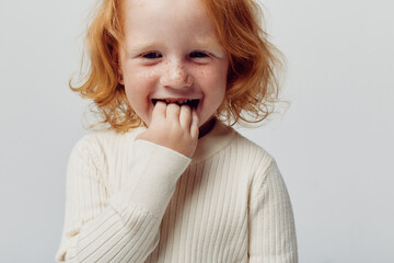 Little girl with red hair holding hand to mouth in front of white background innocent beauty portrait concept