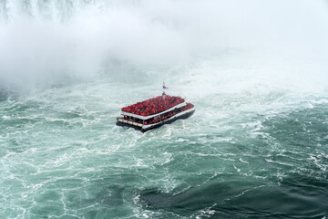 Naklejka premium A tour boat cruises towards to mist at the base of the Horseshoe Falls in Niagara Falls Ontario.