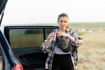 woman wearing a plaid shirt and stands in a field. She puts on a black cap and adjusting it  with one hand. Warm sunset sunlight outdoors in the field