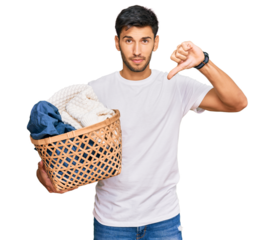 Young handsome man holding laundry basket with angry face, negative sign showing dislike with thumbs down, rejection concept