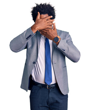 Handsome african american man with afro hair wearing business jacket covering eyes and mouth with hands, surprised and shocked. hiding emotion