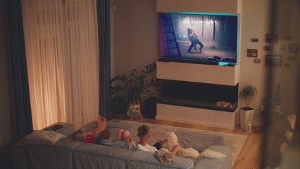 High angle of mother and children lying on sofa with dog and cat in cozy living room and watching...