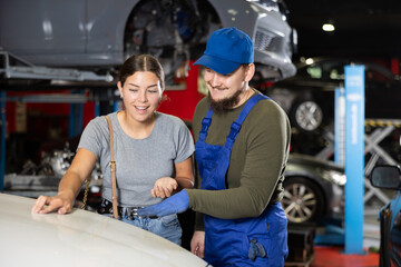 Fototapeta premium Young guy mechanic advises young woman client on repairing of car in car service station