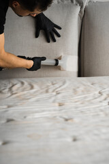 Cleaner is washing off couch from stains, dust and dirt using extractor at home. Dry cleaning of sofa pillows with extractor.