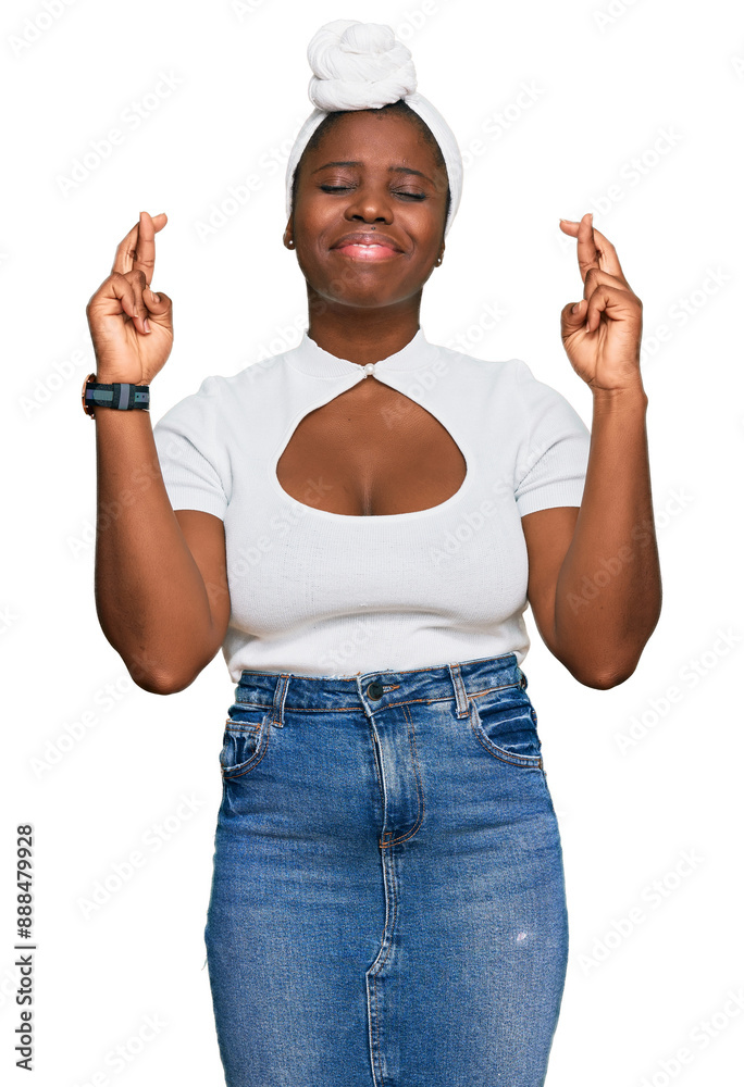 Wall mural Young african woman with turban wearing hair turban over isolated background gesturing finger crossed smiling with hope and eyes closed. luck and superstitious concept.