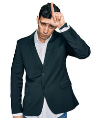 Handsome hispanic man wearing business clothes making fun of people with fingers on forehead doing loser gesture mocking and insulting.