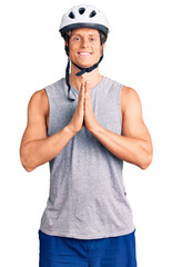 Young handsome man wearing bike helmet praying with hands together asking for forgiveness smiling confident.