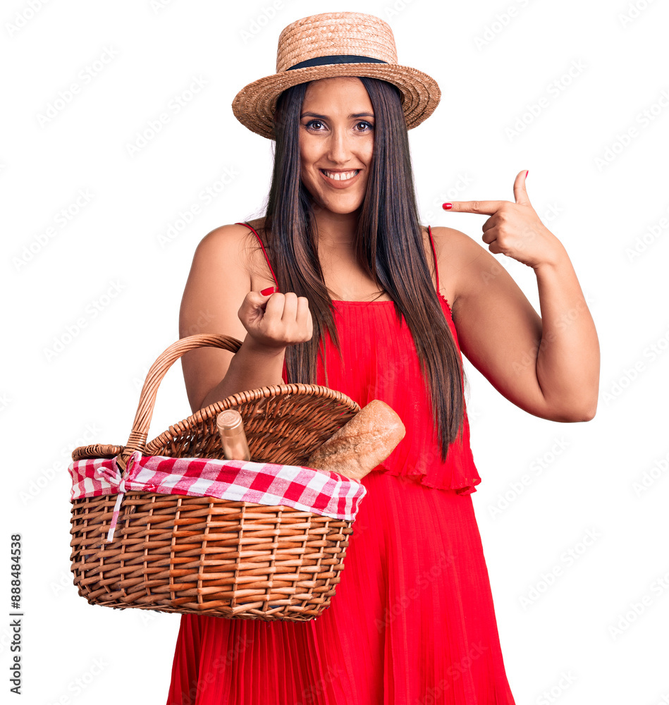 Poster young beautiful brunette woman wearing summer hat holding picnic basket pointing finger to one self 