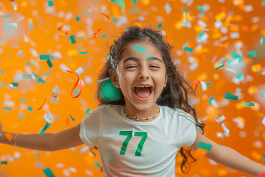 India Independence Day. A happy Indian girl wearing a white t-shirt green text "77" with orange, white and green confetti on orange background. 77th India Independence day