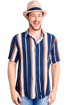 Young handsome caucasian man wearing summer hat winking looking at the camera with sexy expression, cheerful and happy face.