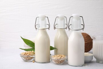 Different types of vegan milk and ingredients on light grey table