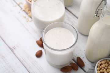 Different types of vegan milk and ingredients on white wooden table, closeup
