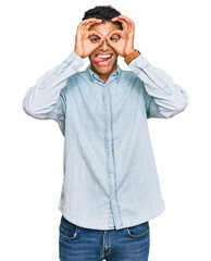 Young handsome african american man wearing casual clothes doing ok gesture like binoculars sticking tongue out, eyes looking through fingers. crazy expression.