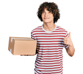 Caucasian teenager holding delivery package smiling happy and positive, thumb up doing excellent and approval sign