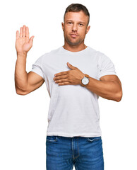Handsome muscle man wearing casual white tshirt swearing with hand on chest and open palm, making a...