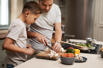 Cooking, father and son in kitchen, cutting vegetables and ingredients with time together, hobby and child development. Parent, dad or boy with nutrition, learning and help with support and skills