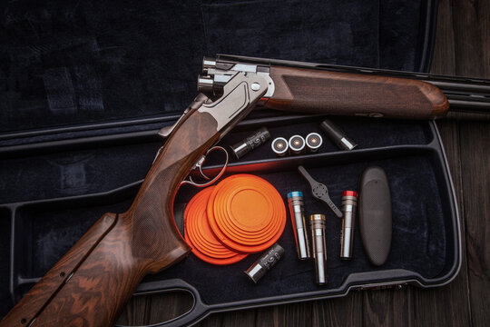Double-barrel luxury shotgun with wooden butt lies in the case. Sport shooting clay pigeons. Shotgun cartridges and chokes. Dark wooden back.