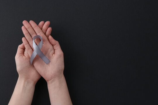 Woman with grey awareness ribbon on black background, top view. Space for text