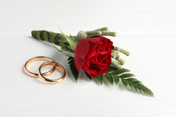 Stylish red boutonniere and rings on white wooden table