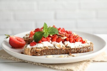Bruschettas with ricotta cheese, chopped strawberries and mint on white wooden table, closeup