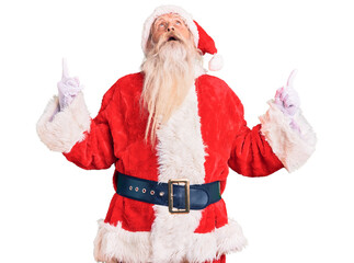 Old senior man with grey hair and long beard wearing traditional santa claus costume amazed and surprised looking up and pointing with fingers and raised arms.
