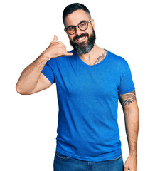 Fototapeta premium Hispanic man with beard wearing casual t shirt and glasses smiling doing phone gesture with hand and fingers like talking on the telephone. communicating concepts.
