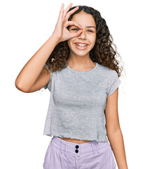 Teenager hispanic girl wearing casual clothes smiling happy doing ok sign with hand on eye looking through fingers