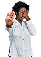 African american woman with afro hair wearing casual white t shirt covering eyes with hands and doing stop gesture with sad and fear expression. embarrassed and negative concept.