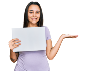 Young hispanic woman holding blank empty banner celebrating victory with happy smile and winner expression with raised hands
