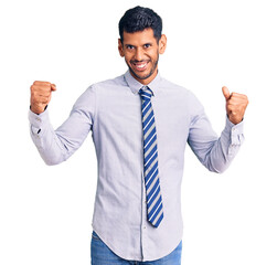 Young latin man wearing business clothes screaming proud, celebrating victory and success very excited with raised arms