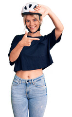 Young beautiful blonde woman wearing bike helmet smiling making frame with hands and fingers with happy face. creativity and photography concept.