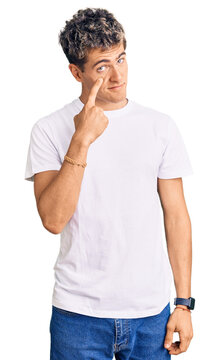 Young handsome man wearing casual white tshirt pointing to the eye watching you gesture, suspicious expression